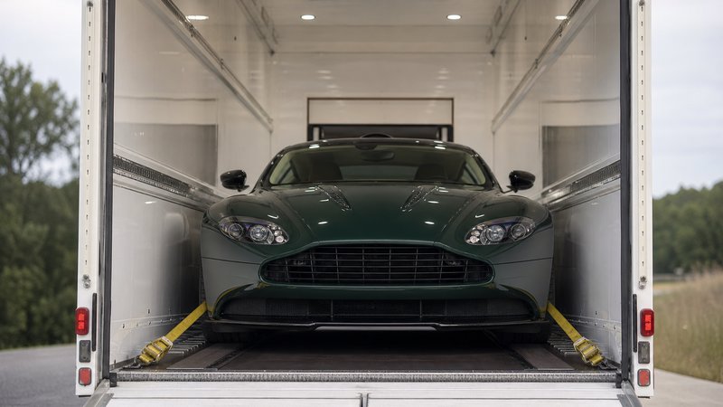 A British racing green Aston Martin strapped down inside an enclosed auto transport trailer, seen from the open rear door