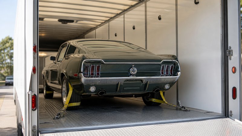 A classic Ford Mustang fastback strapped down inside an enclosed trailer
