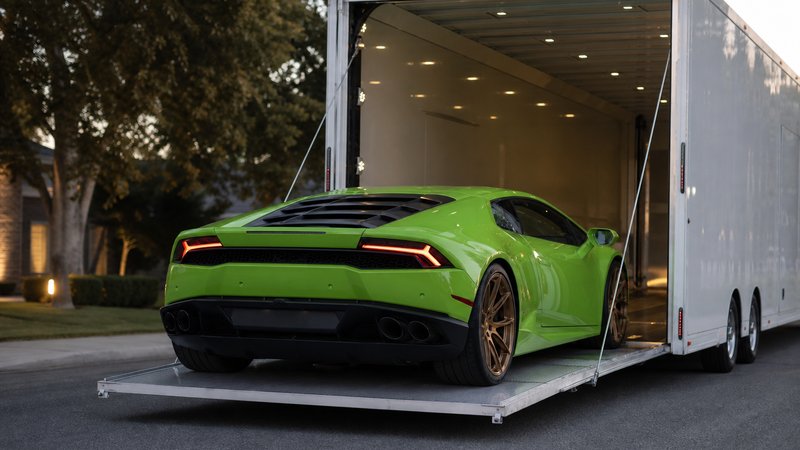 A lime-green Lamborghini on the lowered liftgate of an enclosed auto transport trailer at dusk