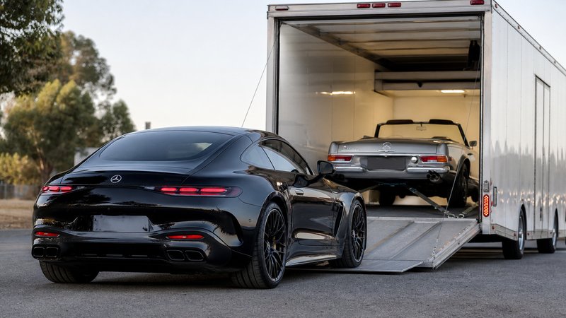 A modern Mercedes-AMG coupe entering an enclosed trailer with a vintage SL already inside