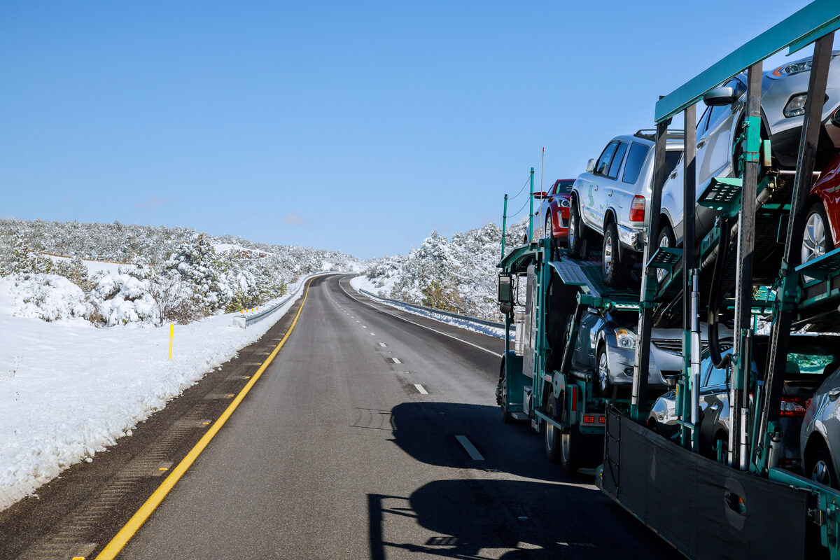 Winter car shipping: a loaded open car carrier on a cleared highway with snow banked on the shoulders